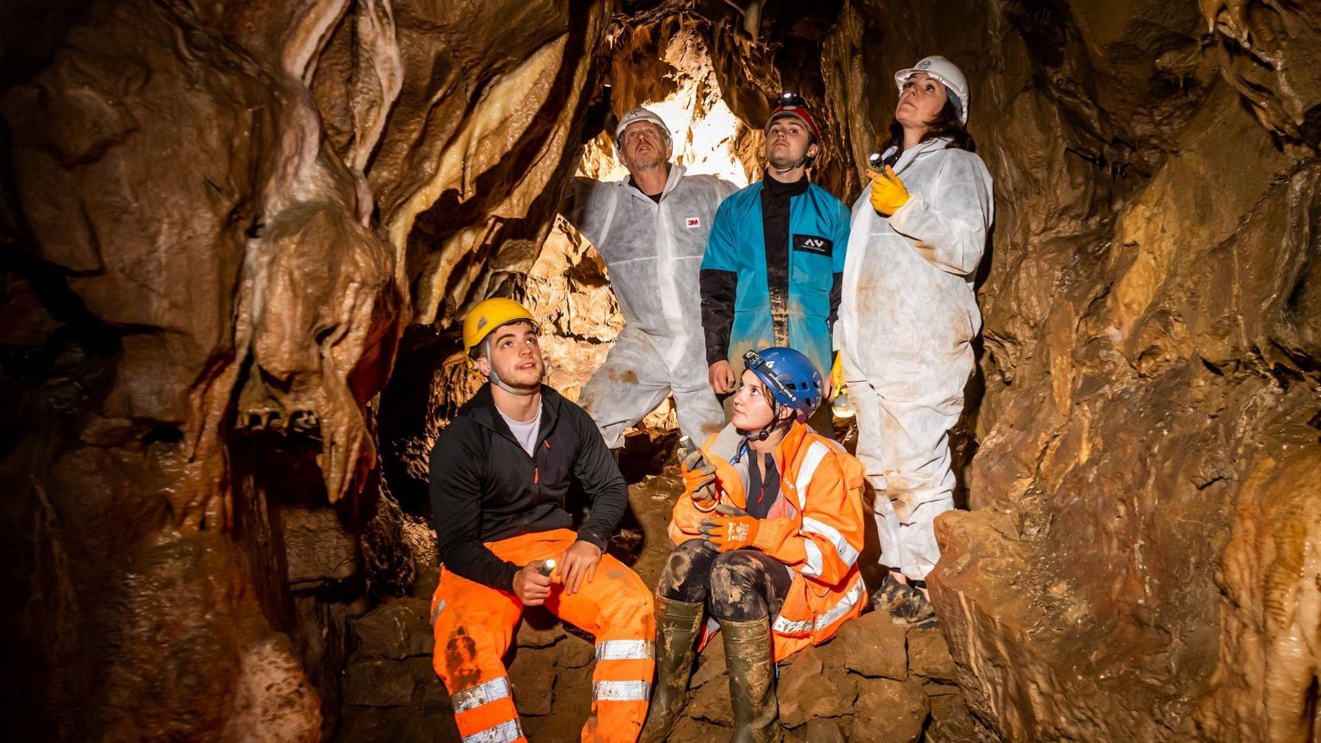 Members of the Bowerman family wearing mud-splattered caving over-suits, helmets and head torches in the new cave