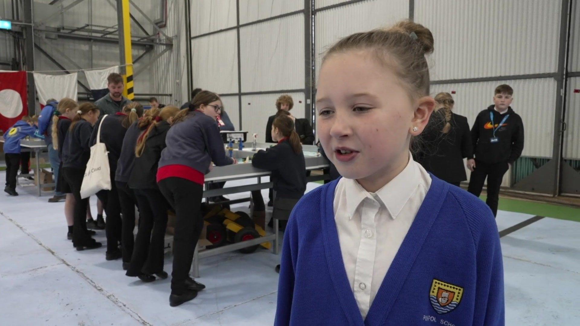 A young girl in blue school uniform standing in front of a group of other children around a table