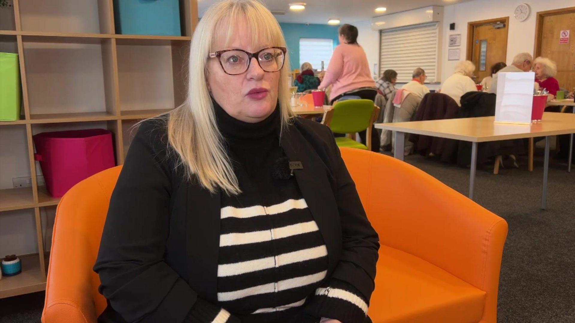 Lesley Nowell Hitchcock from Age UK being interviewed by the BBC. She wears a black jacket and a black sweater with white stripes across it.