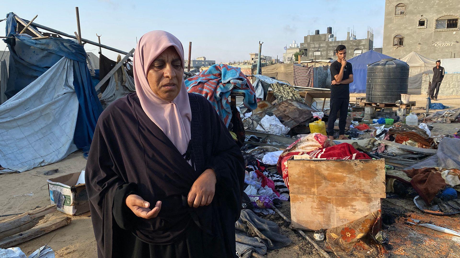 A Palestinian woman looks down towards the camera as she inspects damage to a camp housing displaced people in Khan Younis, after an Israeli strike on 2 July. Other people, broken tents and strewn belongings can be seen in the background against a blue sky.