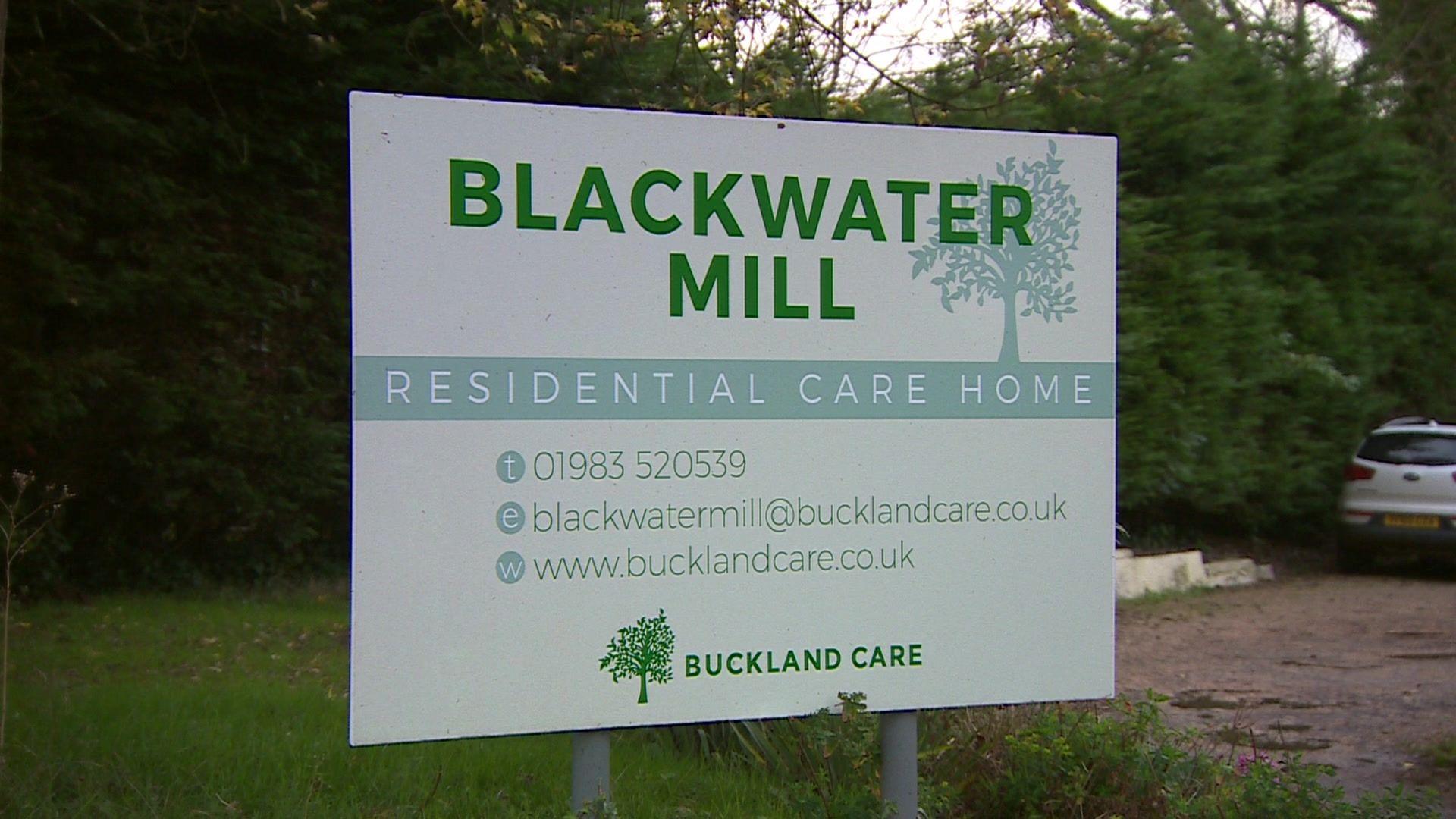 A pale green sign that says 'Blackwater mill' in large green writing. Behind it is a car park and a grass lawn.