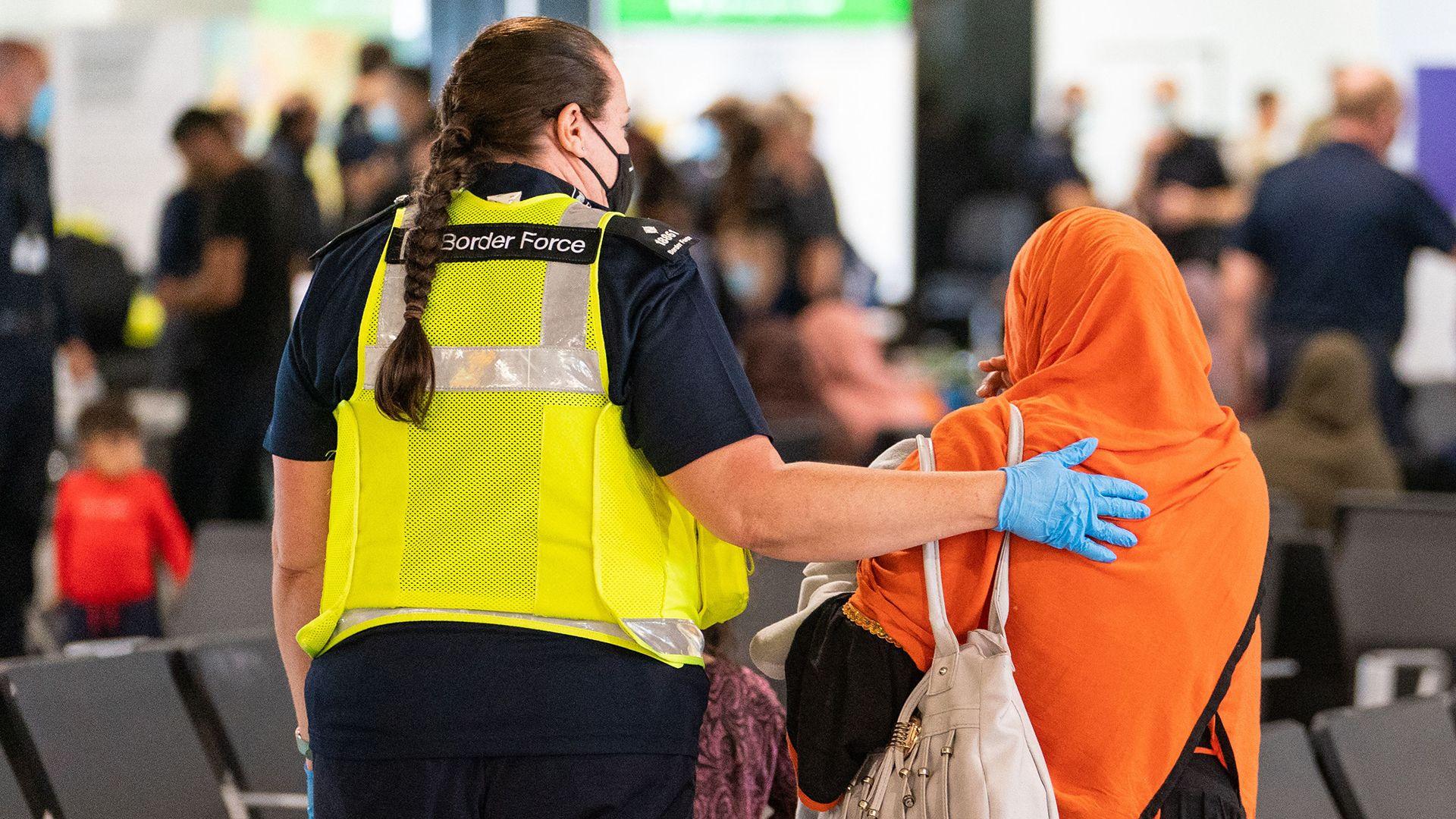 A member of Border Force staff wearing reflective jacket assists an Afghan refugee wearing an orange hijab and places an arm on her shoulder on her arrival on an evacuation flight from Afghanistan, at Heathrow Airport, London on August 26, 2021.