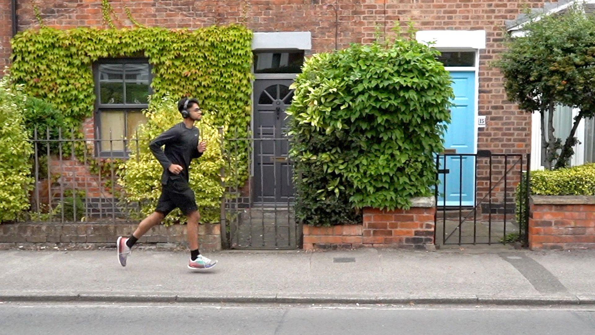 Mridul is running along a residential street with his headphones on.