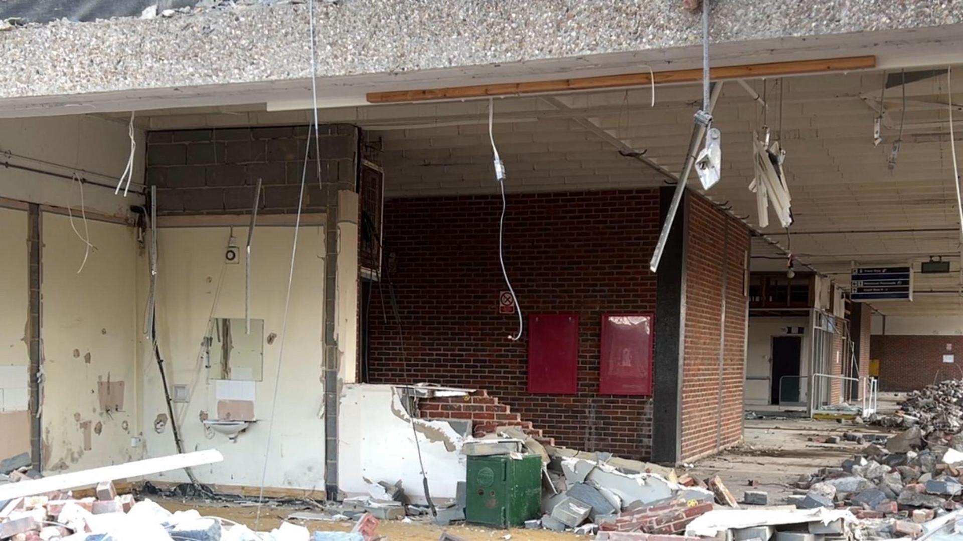 Picture shows a half demolished wall with a sink hanging off it and a large green safe - about a metre tall surrounded by rubble.