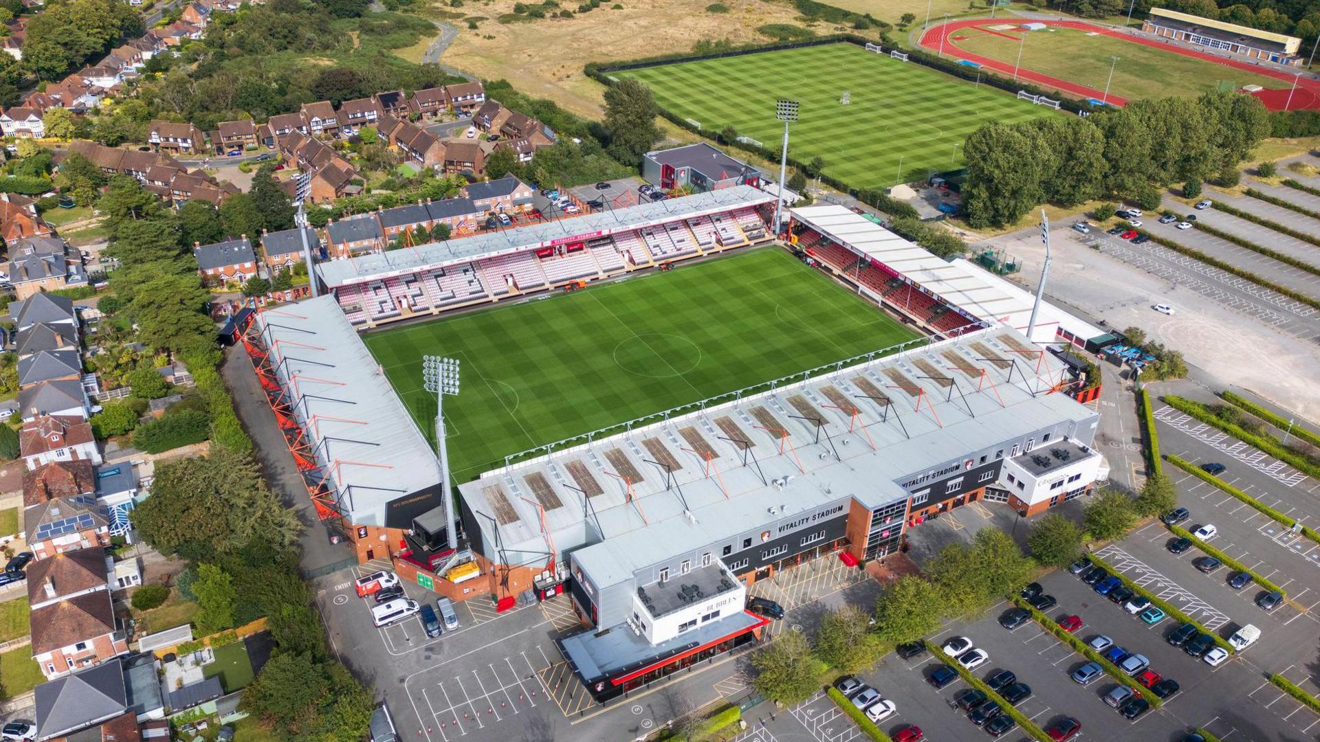 A bird's eye view of Vitality Stadium in Bournemouth, surrounded by sports pitches, a car park and homes 