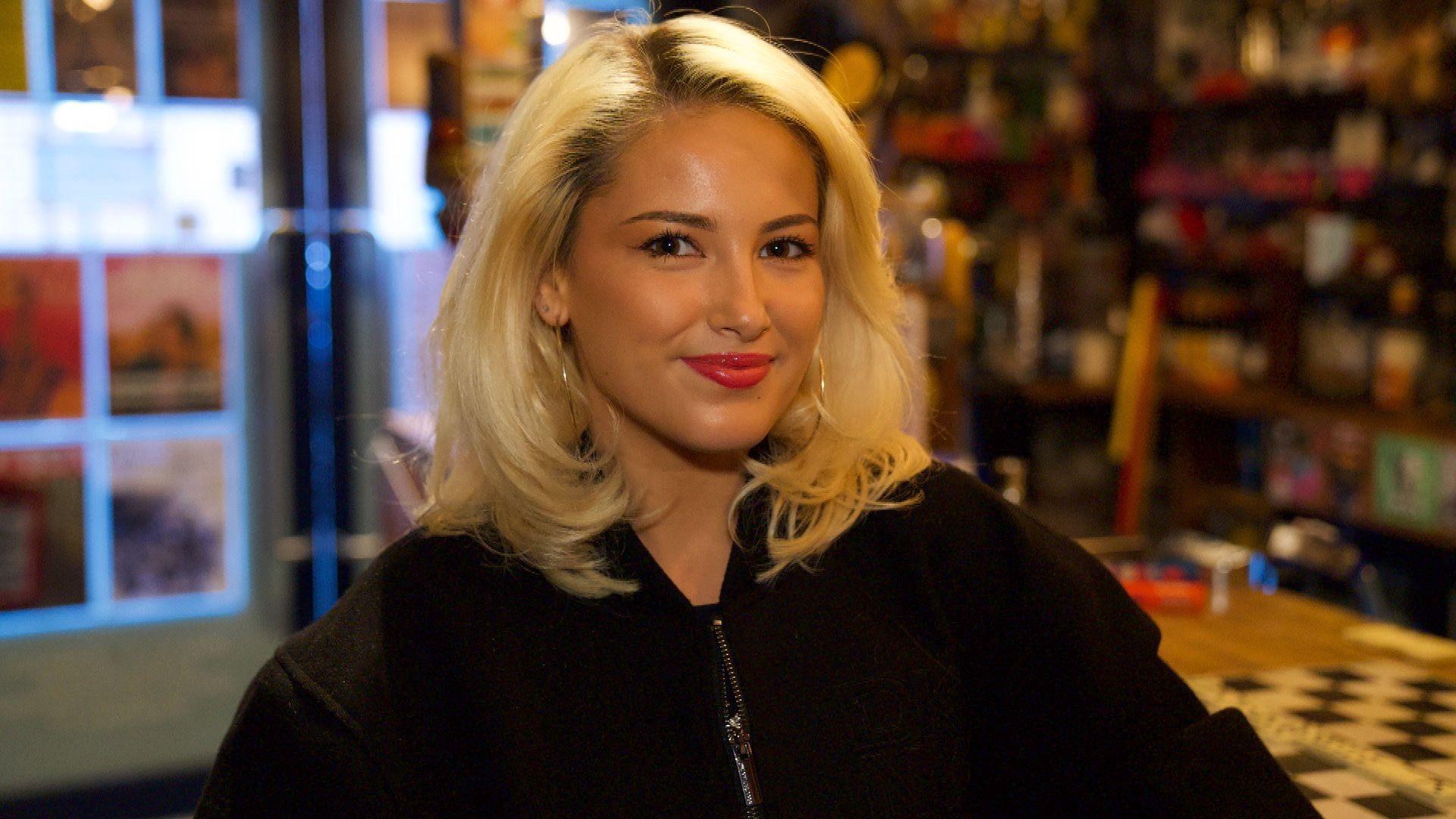 A young woman smiling at the camera. She is wearing a black zip-up hoodie.