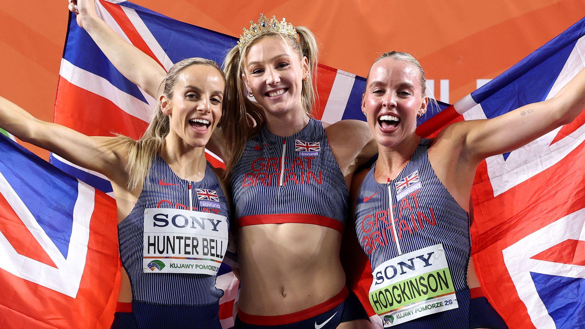 (L-R) Georgia Hunter Bell, Molly Caudery and Keely Hodgkinson pose for a photo at the World Athletics Indoor Championships. They're holding union jack flags behind them and wearing Team GB athletic wear