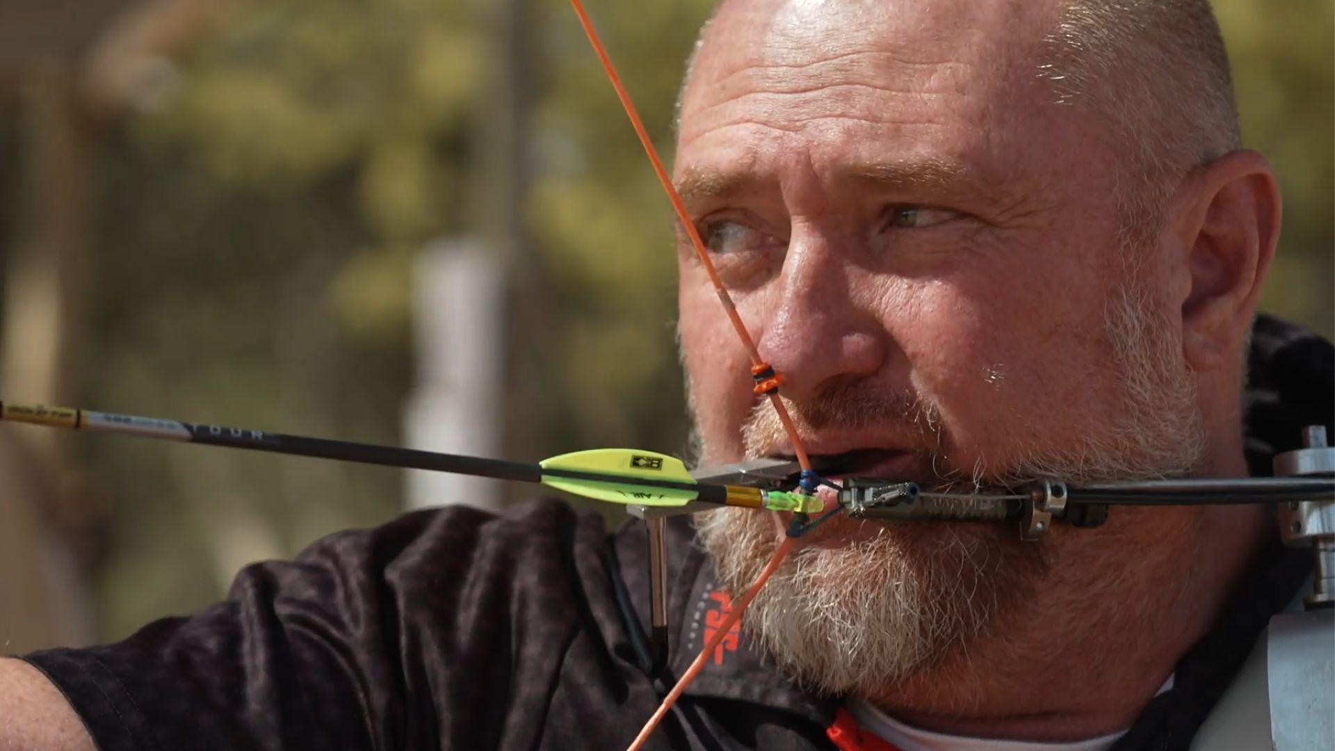 Para archer has arrow in his mouth preparing to shoot at the target