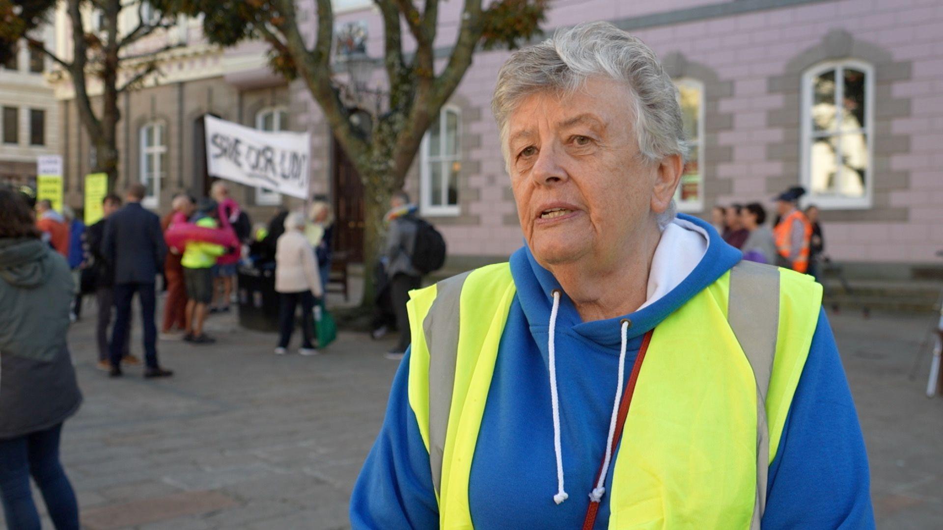 Carole Penfold is wearing a high-vis jacket and a blue hoodie. She is in Jersey's Royal Square 