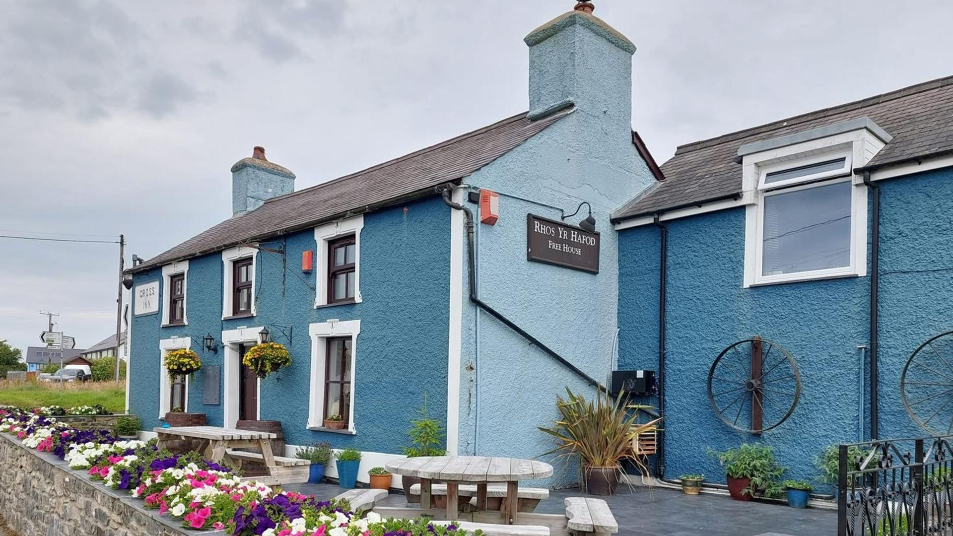 Llun o du allan i'r dafarn yn Llanon. Mae'r dafarn wedi'i phaentio'n las ac mae rhes o flodau lliwgar y tu allan iddi.