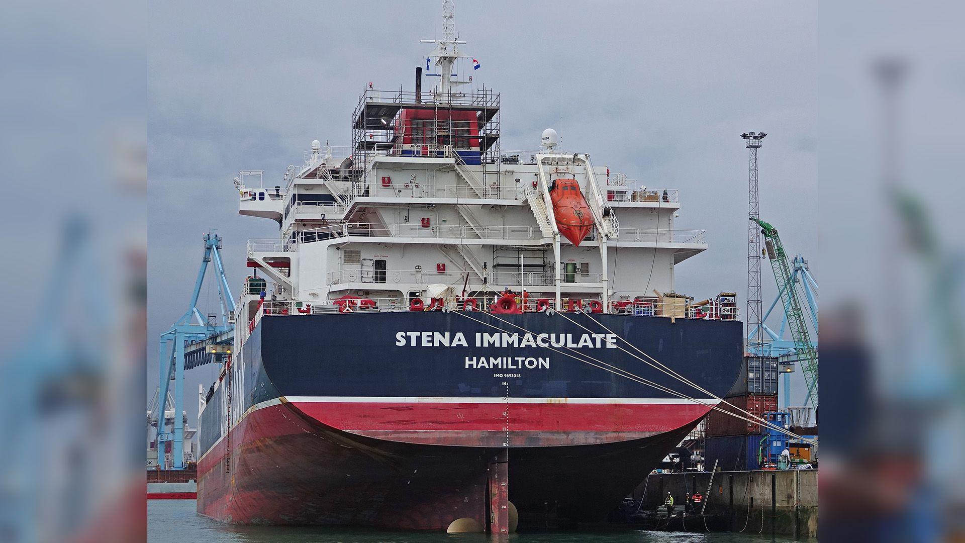 The Stena Immaculate has a read and navy blue hull of the boat. It has white structures on top 