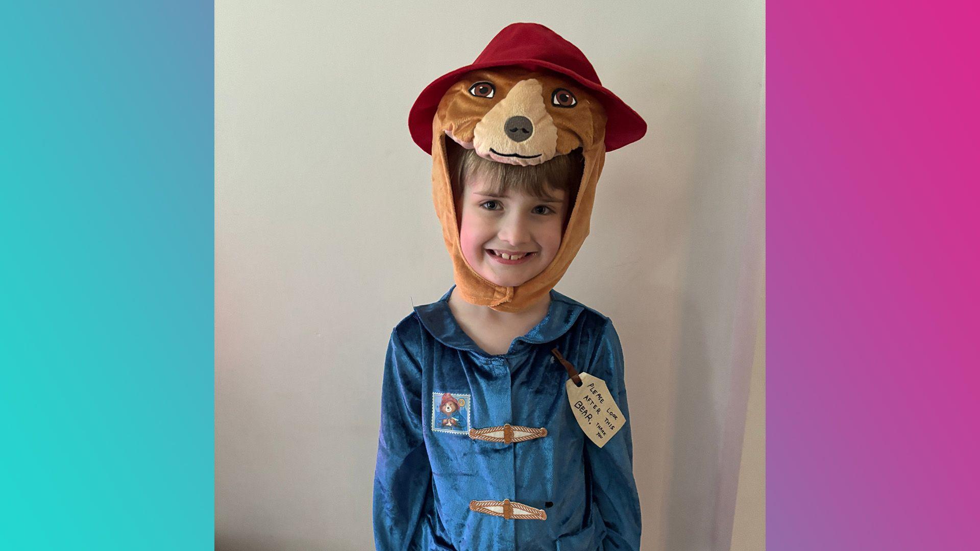 Paddington Bear's face and hat is sitting on top of Dylan's head as part of a headpiece. He is also wearing a blue top with toggles and a label, just like Paddington Bear