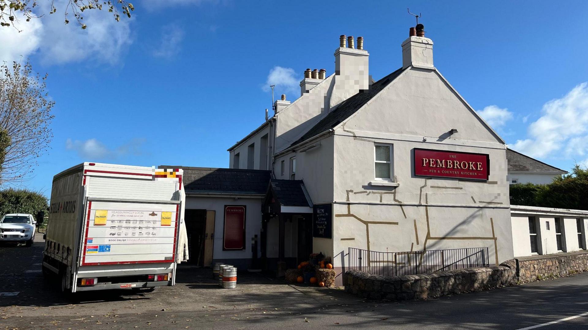 A white lorry delivering kegs of beer is parked outside the Pembroke pub in Jersey, which has white walls and a red name sign.