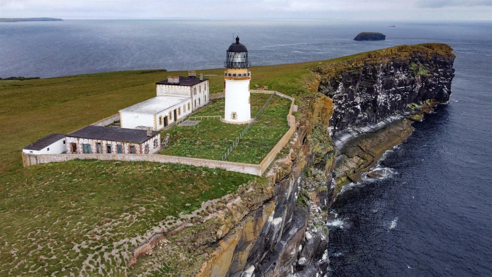 Aerial view image of a small island with a white tower lighthouse and four buildings, surrounded by a wall