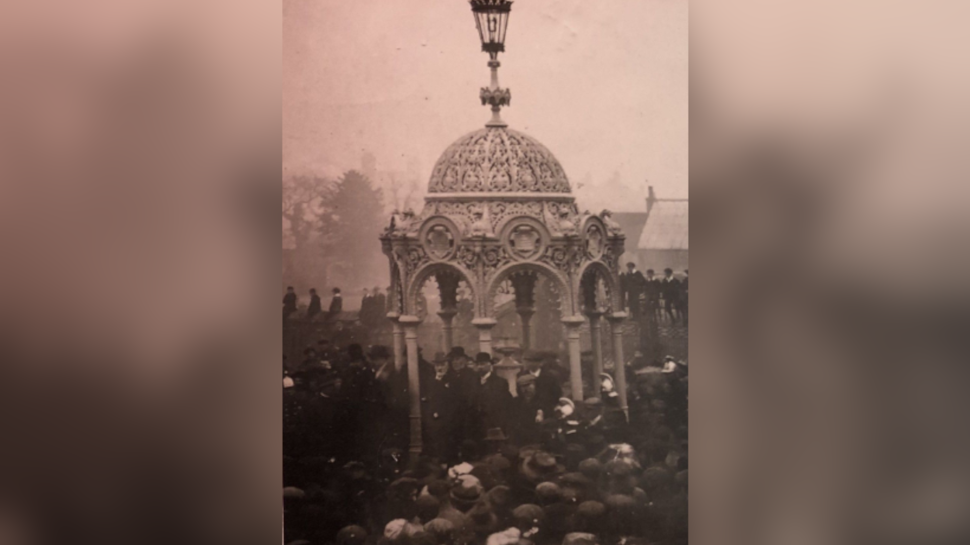 Black and white picture from 1912 of big crowds gathered around a domed monument complete with water drinking feature in the centre. The structure is ornate, with eight open sides with arches and eight pillars supporting the dome. It stands about 8m (25ft) high and has a Victorian looking gas lamp on the top.