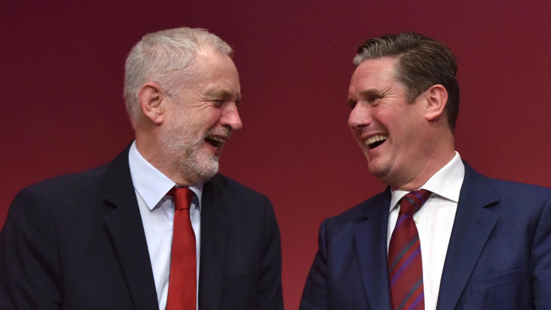 Jeremy Corbyn and Sir Keir Starmer look at each other laughing.