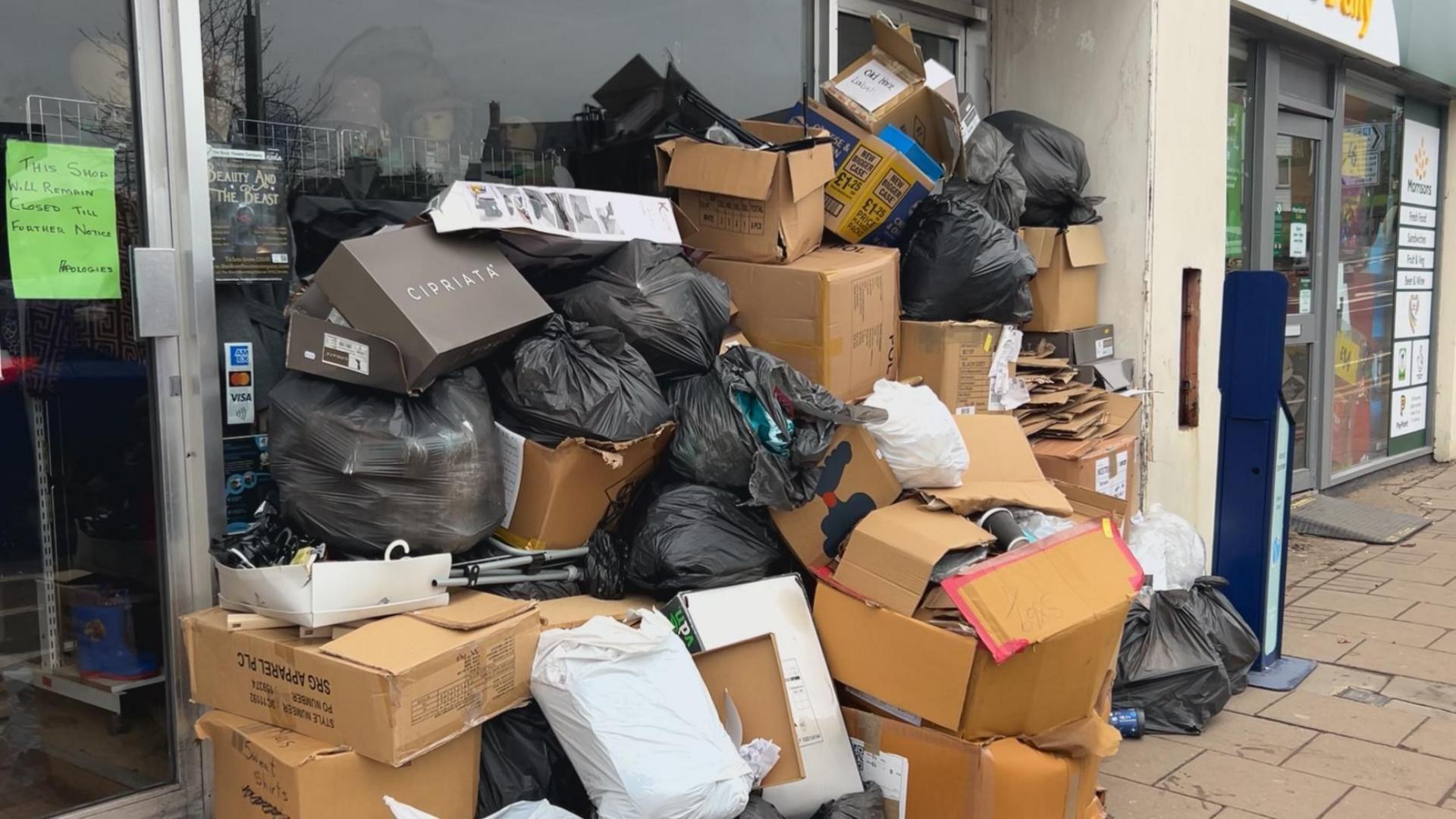 A clothing shop, closed until further notice, with dozens of wet boxes and bags of clothes piled on top of each other out the front.