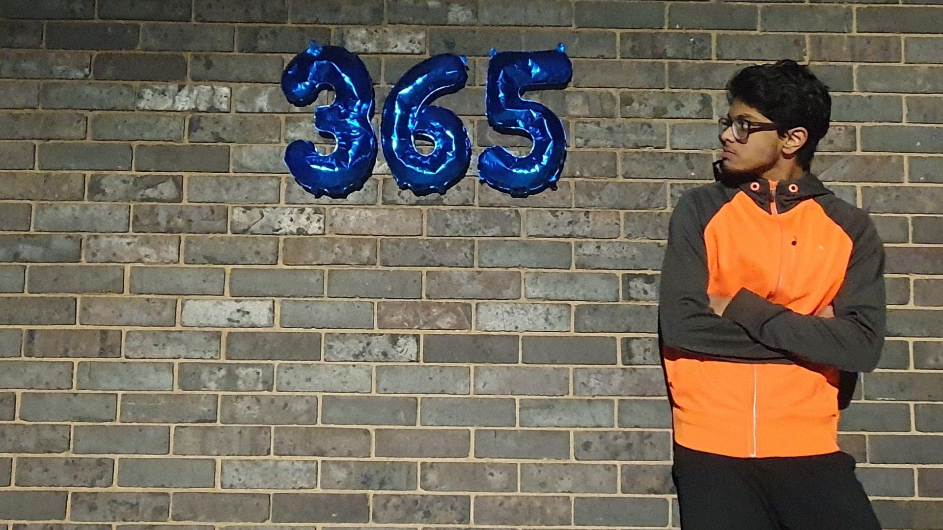 Mridul is leant against a wall looking at balloons that make up the number 365 