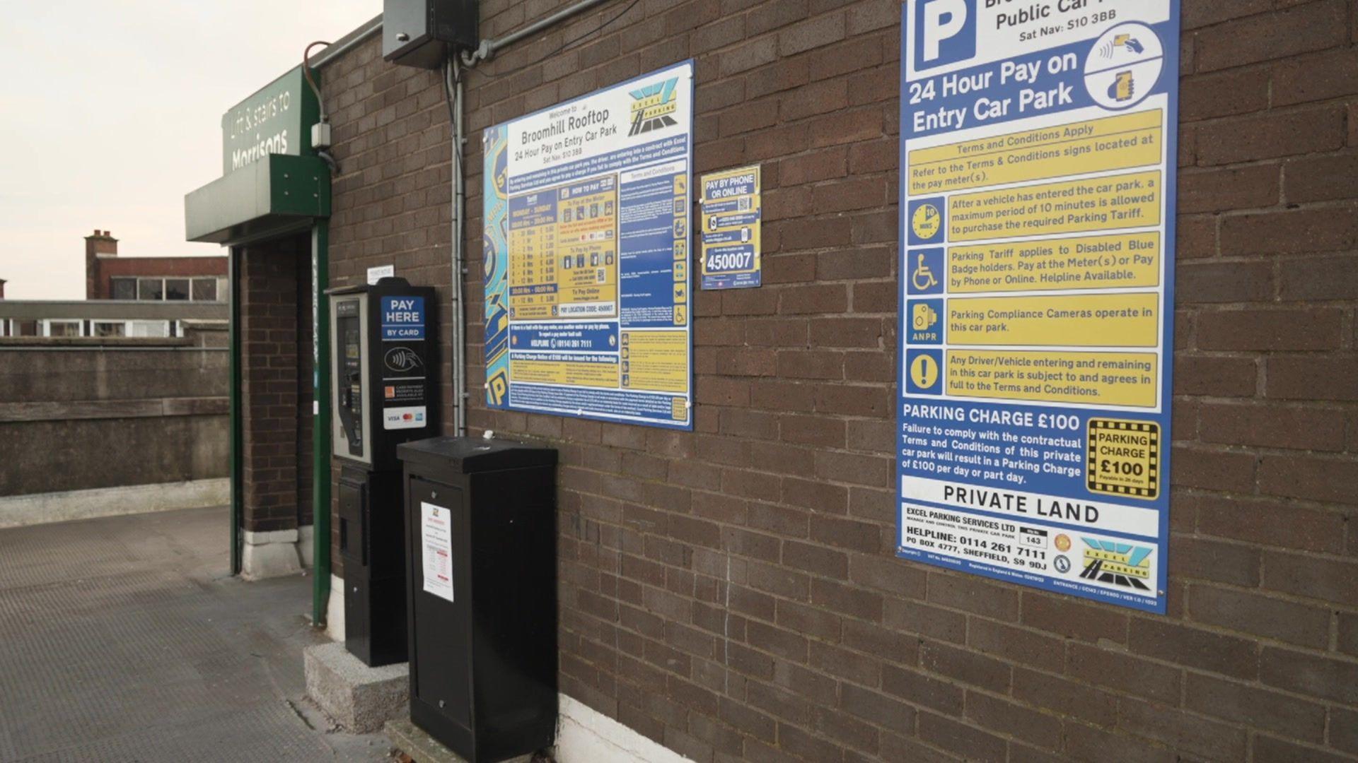 A parking metre with two boards explaining parking rules at a car park