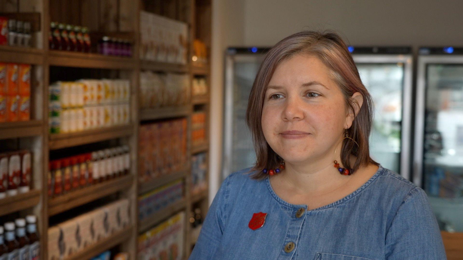 Alice Nunn from the Salvation Army, wearing a blue dress, with a red Salvation Army crest pin badge on her right chest, standing in a shop