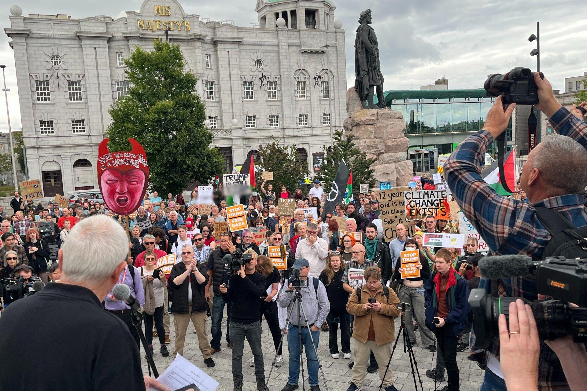 Several hundred anti-Trump protesters with placards in Aberdeen - journalists at the right of the frame point cameras at the crowd