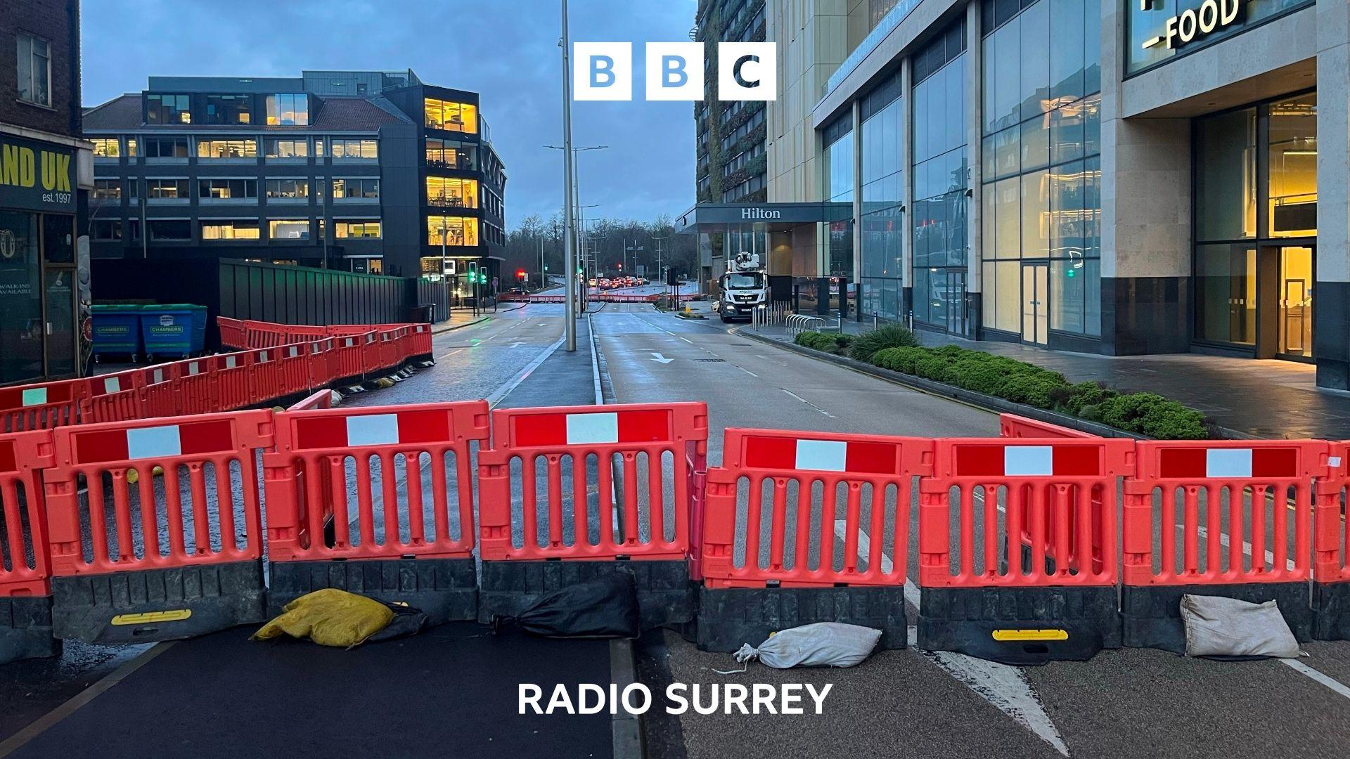 A line of plastic red barriers sit across a closed road in Woking town centre. 