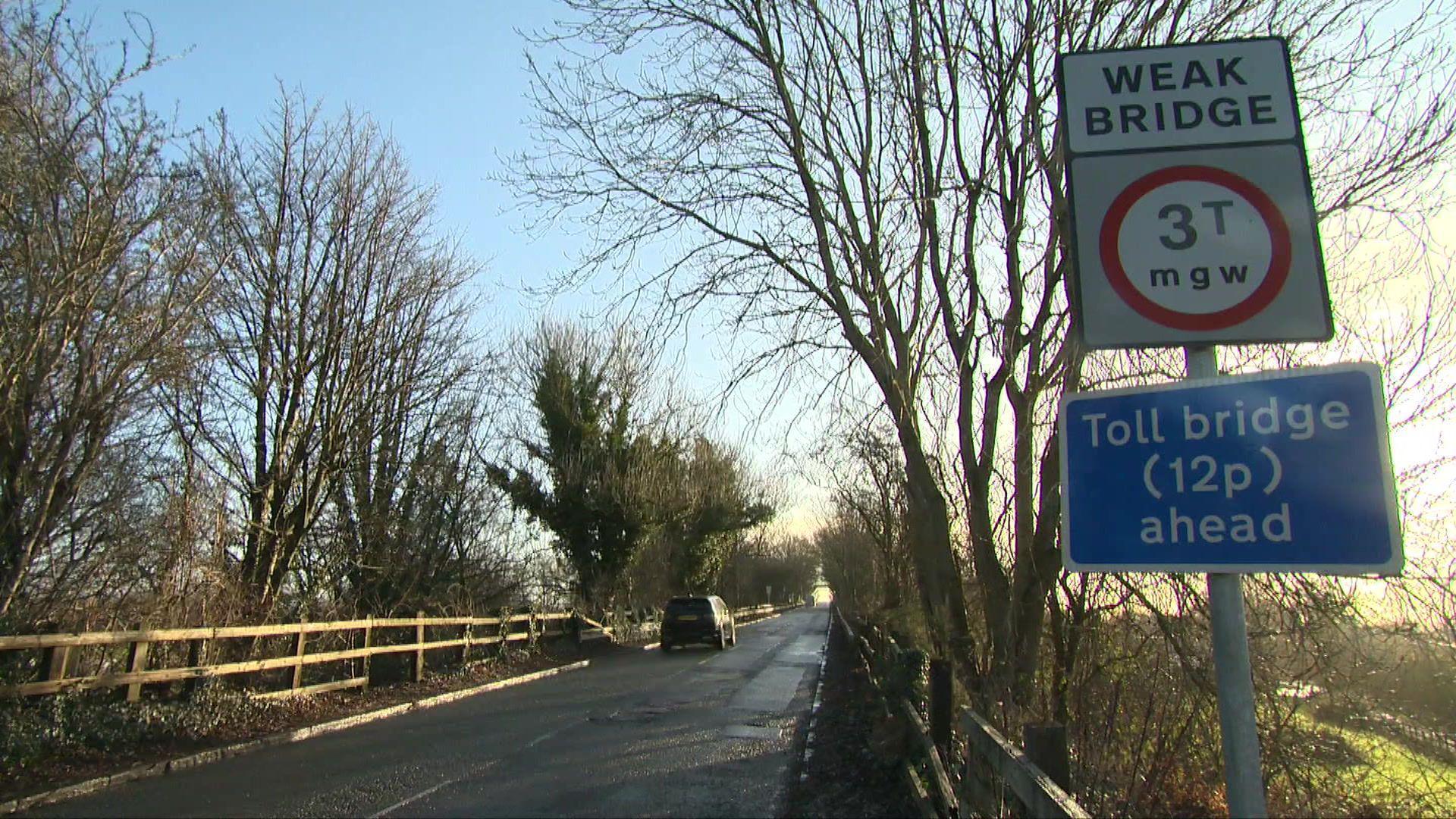 A view of the road leading to Warburton Toll Bridge. There is a sign advising the  toll bridge costs 12p to cross.