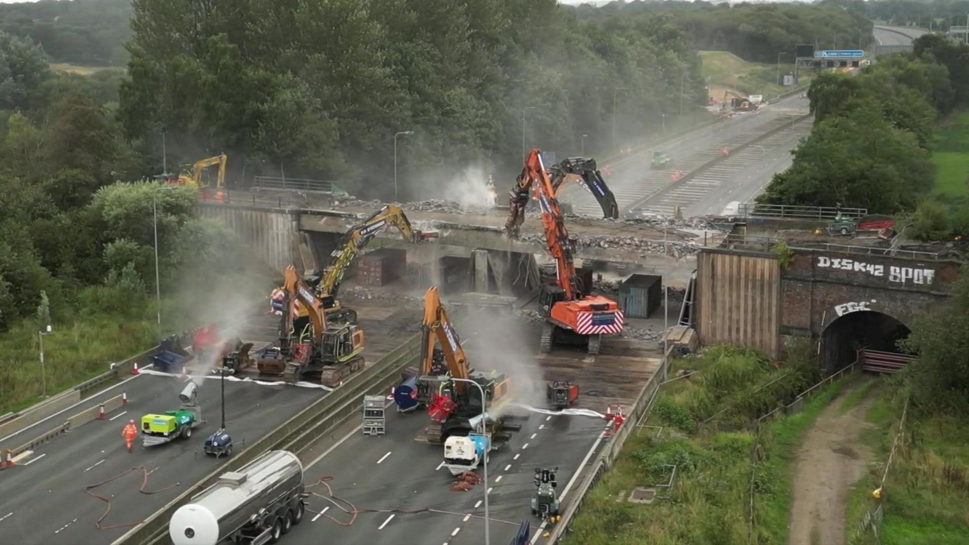 A number of bulldozers start to bring down the bridge