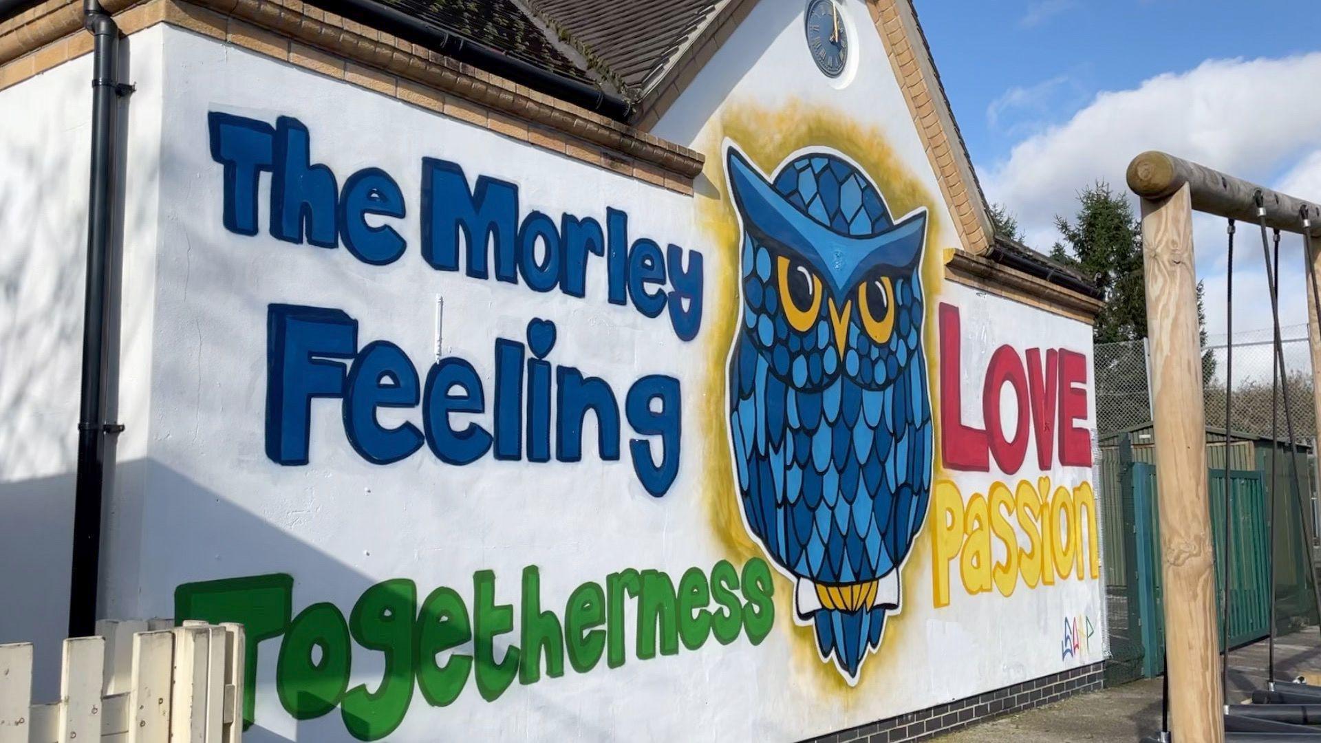 A white wall with a blue cartoon owl and the words love, passion, togetherness and 'The morley feeling' 