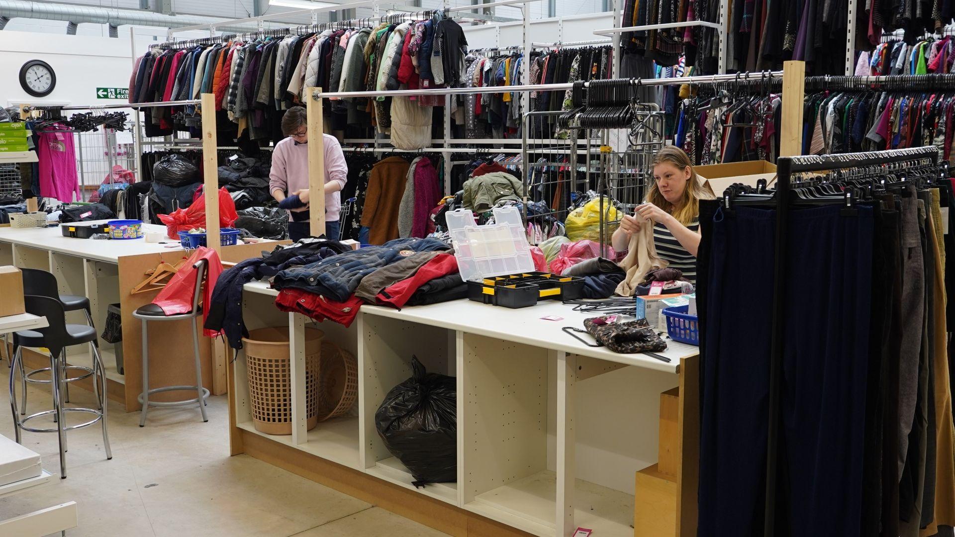 Two people working on a bench full of clothes