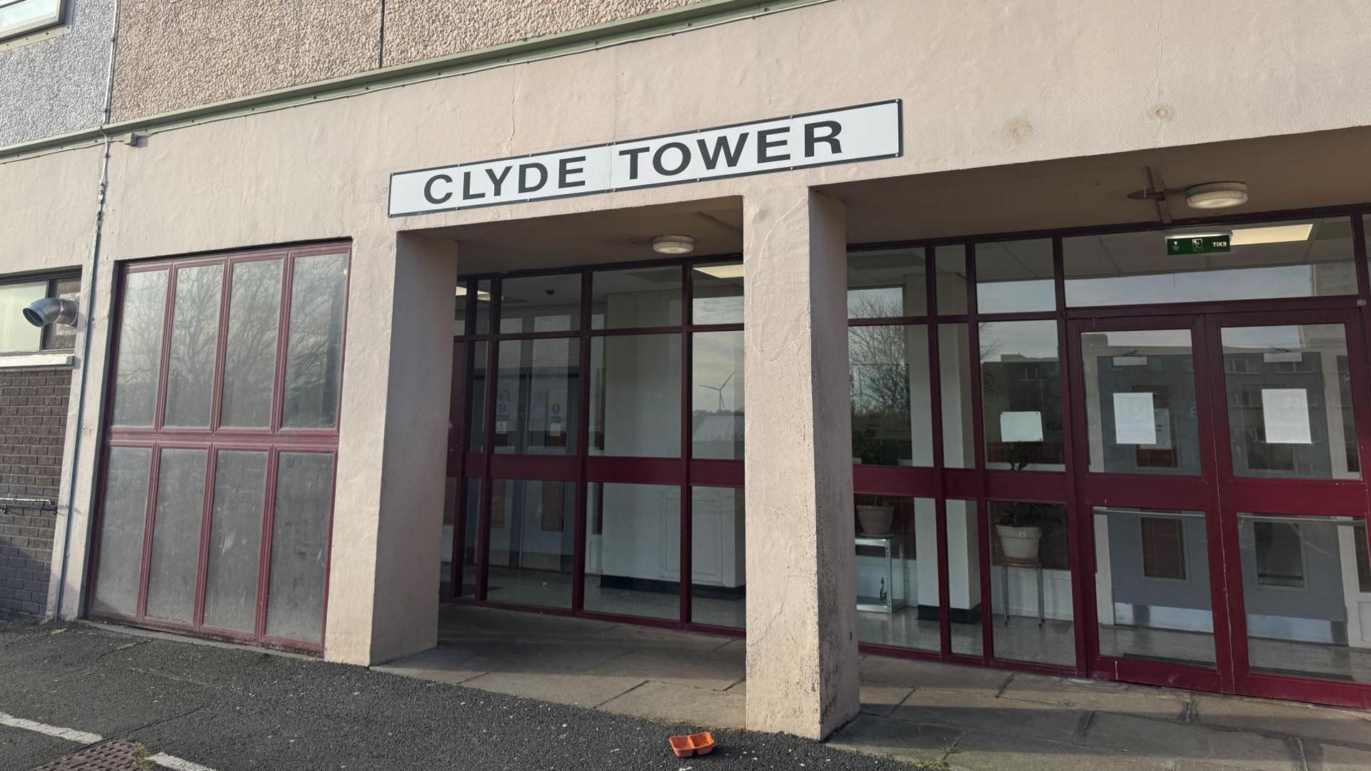 Exterior of a high rise block with glass door entryway and a white sign overhead reading "Clyde Tower"