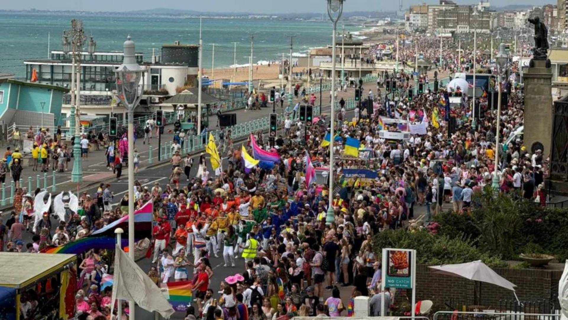 Thousands of people walking from Hove to Brighton along the seafront road. To the left is the sea and beach