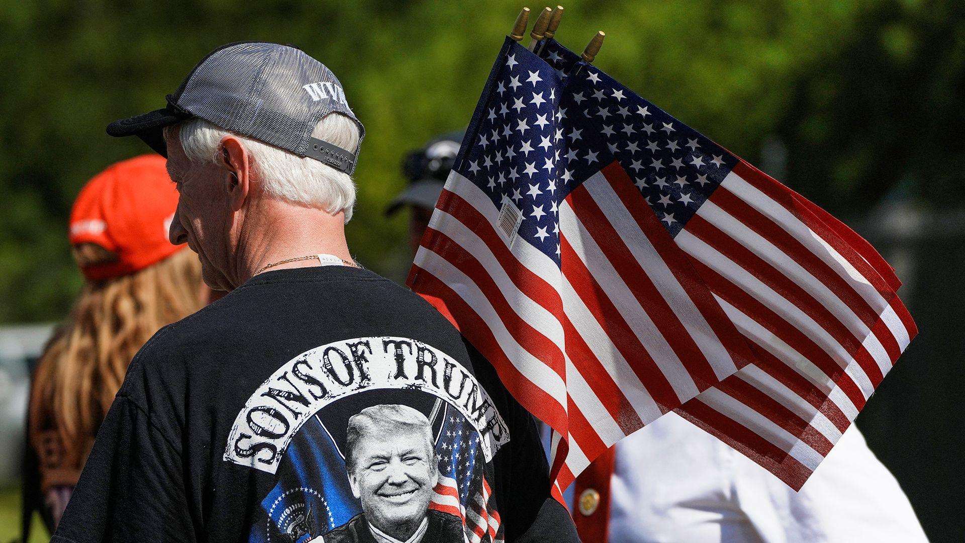 A man stands with his back to the camera holding an American flag while wearing a Trump T-shirt at a rally in Pittston on 16 July.