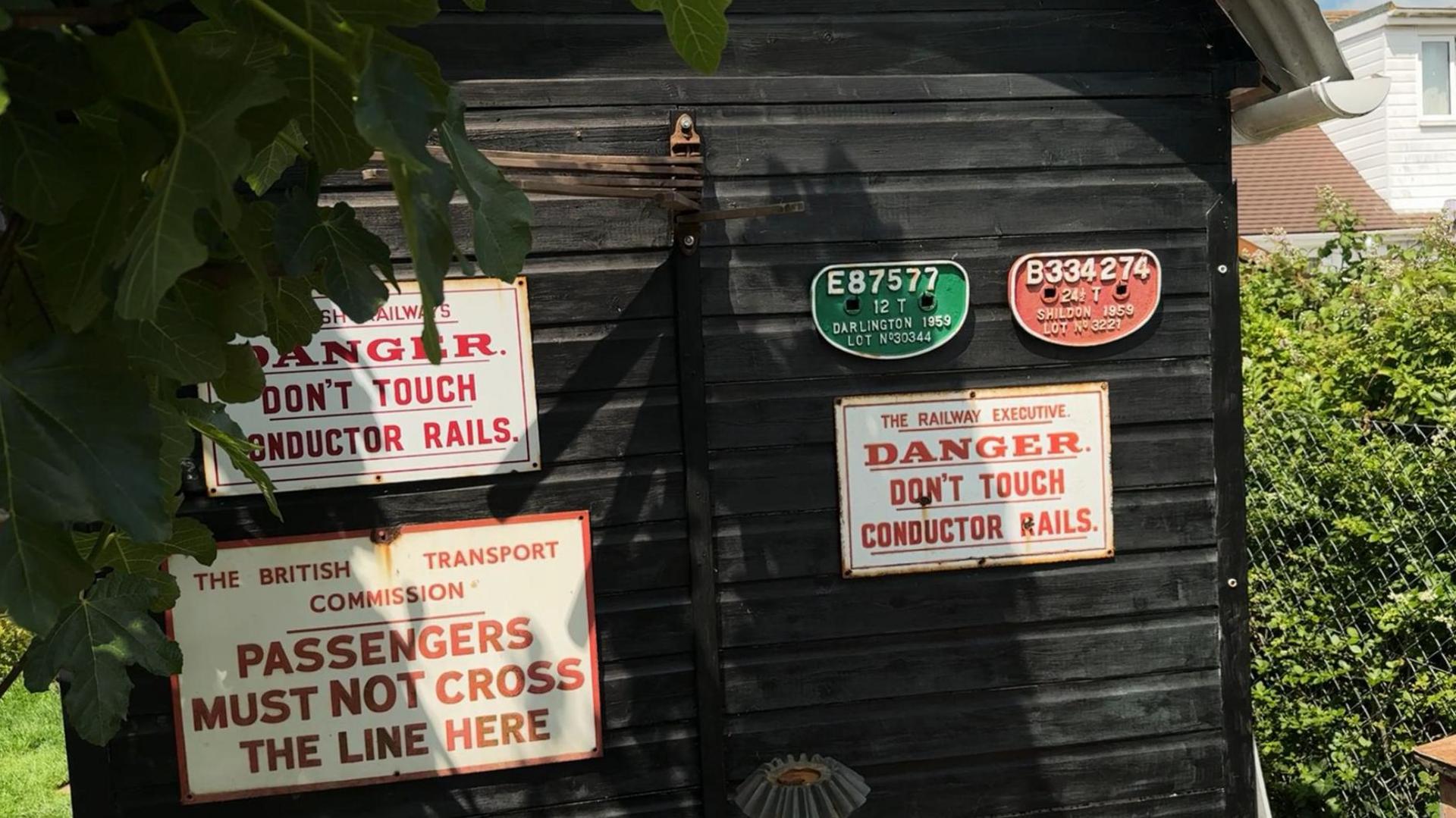 Signage on Adrian's garden workshop which says "danger don't touch conductor rails" and "passengers must not cross the line here".