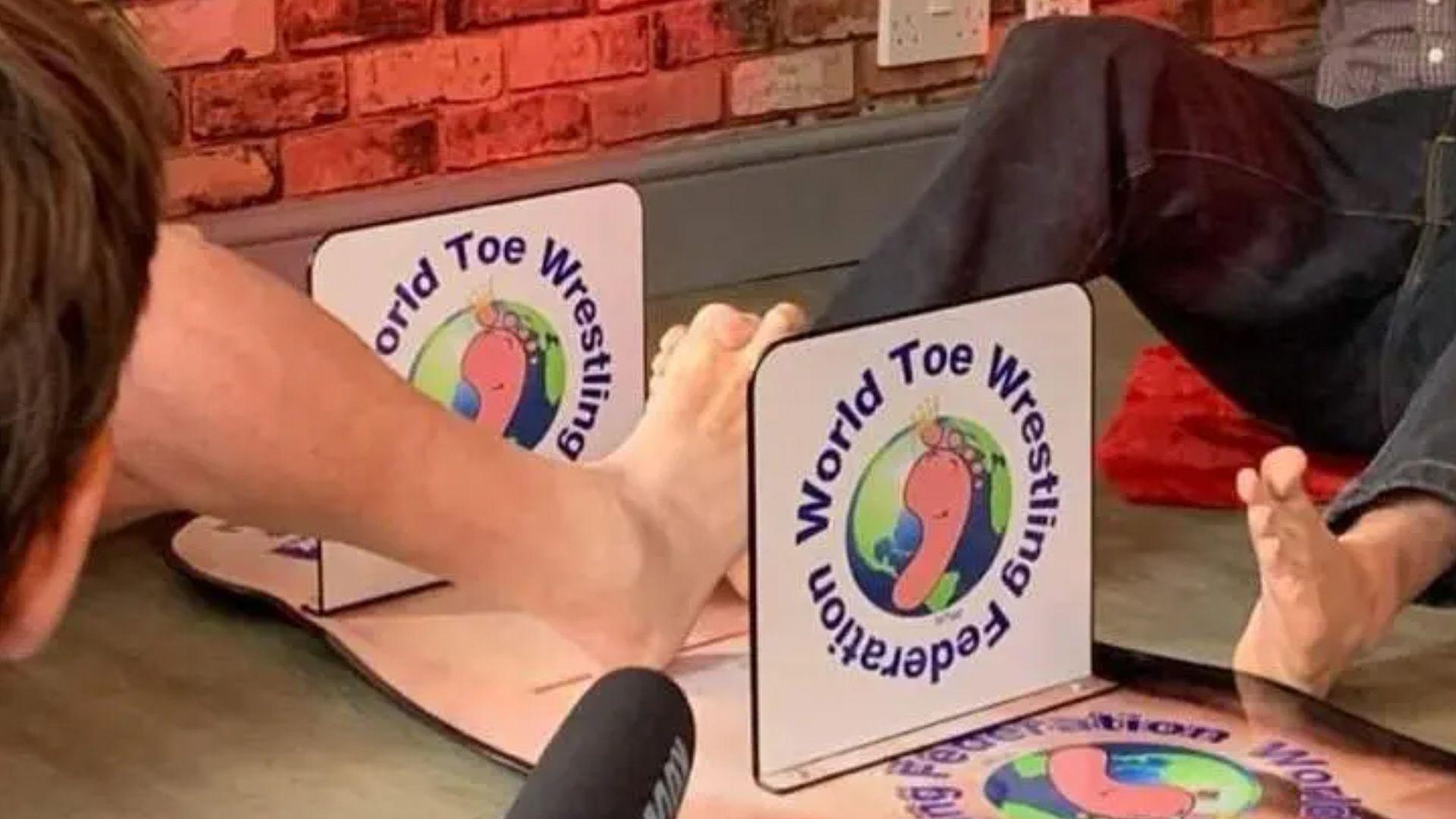 World Toe Wrestling Championship tournament taking place in Fenny Bentley, with two competitors locking their toes together on the 'toedium'.