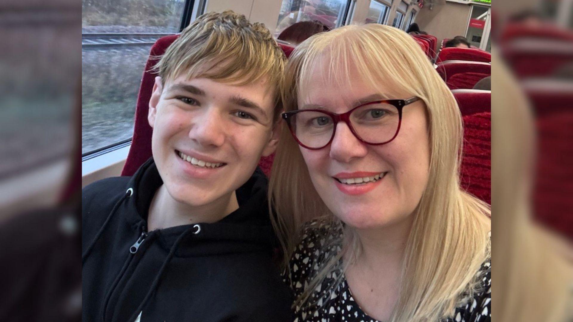 Freddie with his mum Sarah on a train, smiling for a selfie.