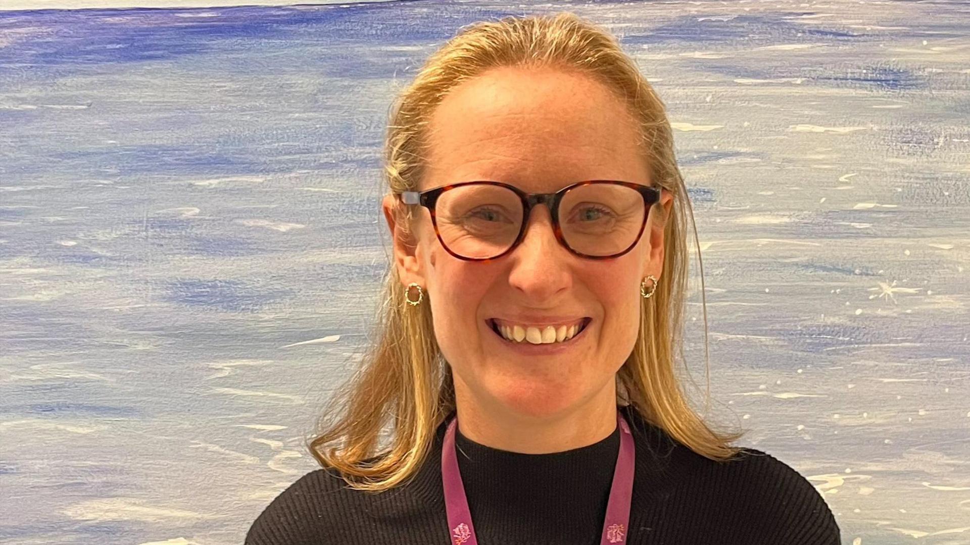 Headshot of Dr Chrissie Parfitt who is wearing a black top, maroon lanyard and glasses. She has blonde hair.