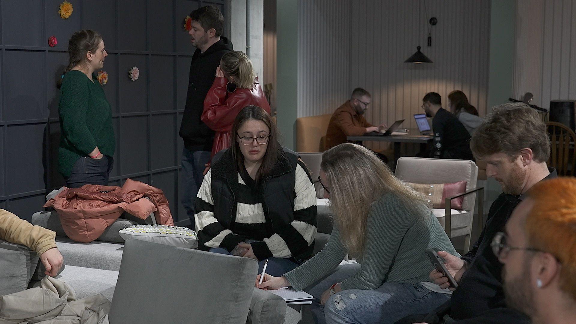 Residents sat on seats in a cafe. Some look at laptops, pieces of paper, and phones.