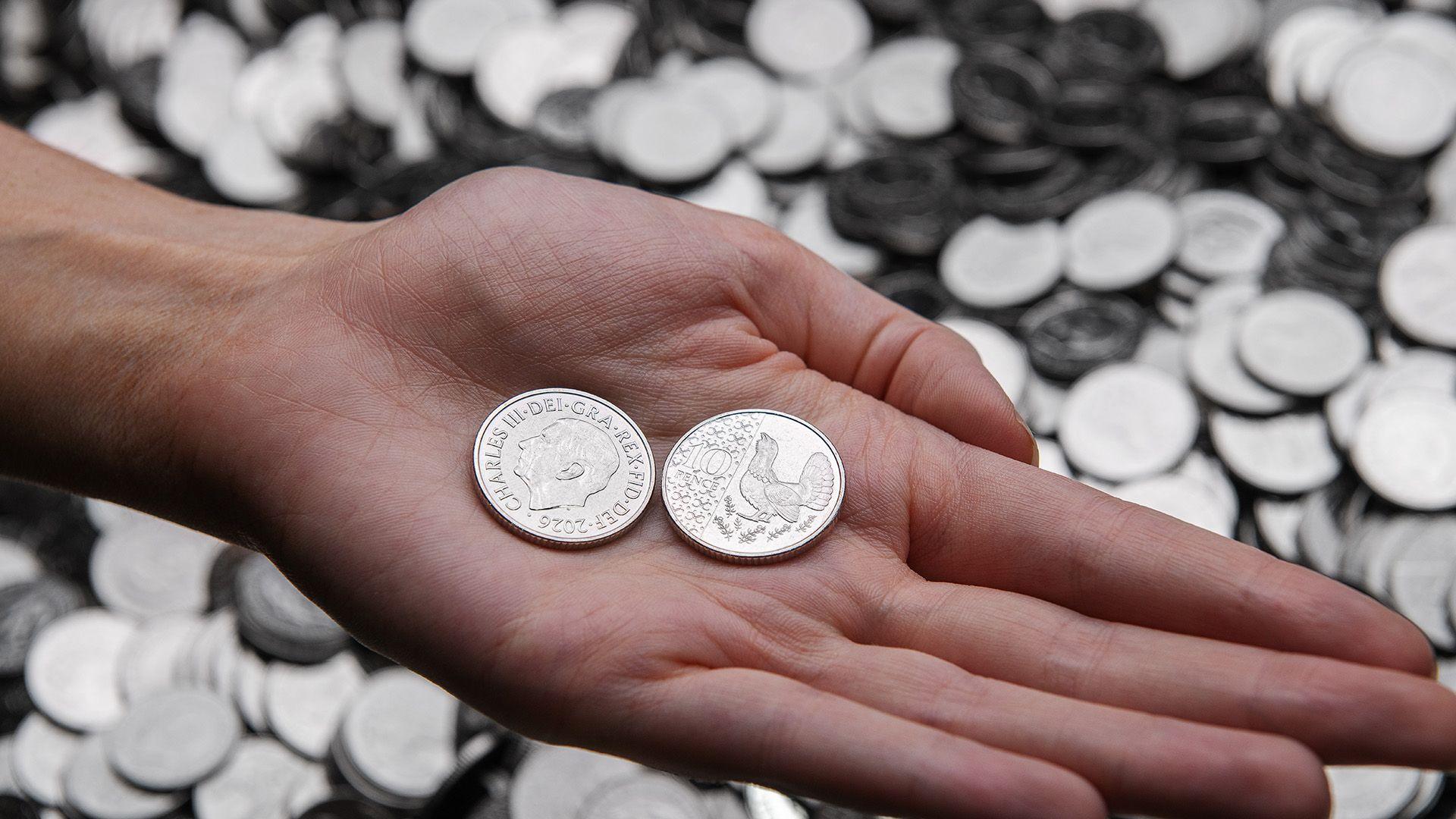 A hand on a background of coins holding two coins , one with the King's head and one with a bird.