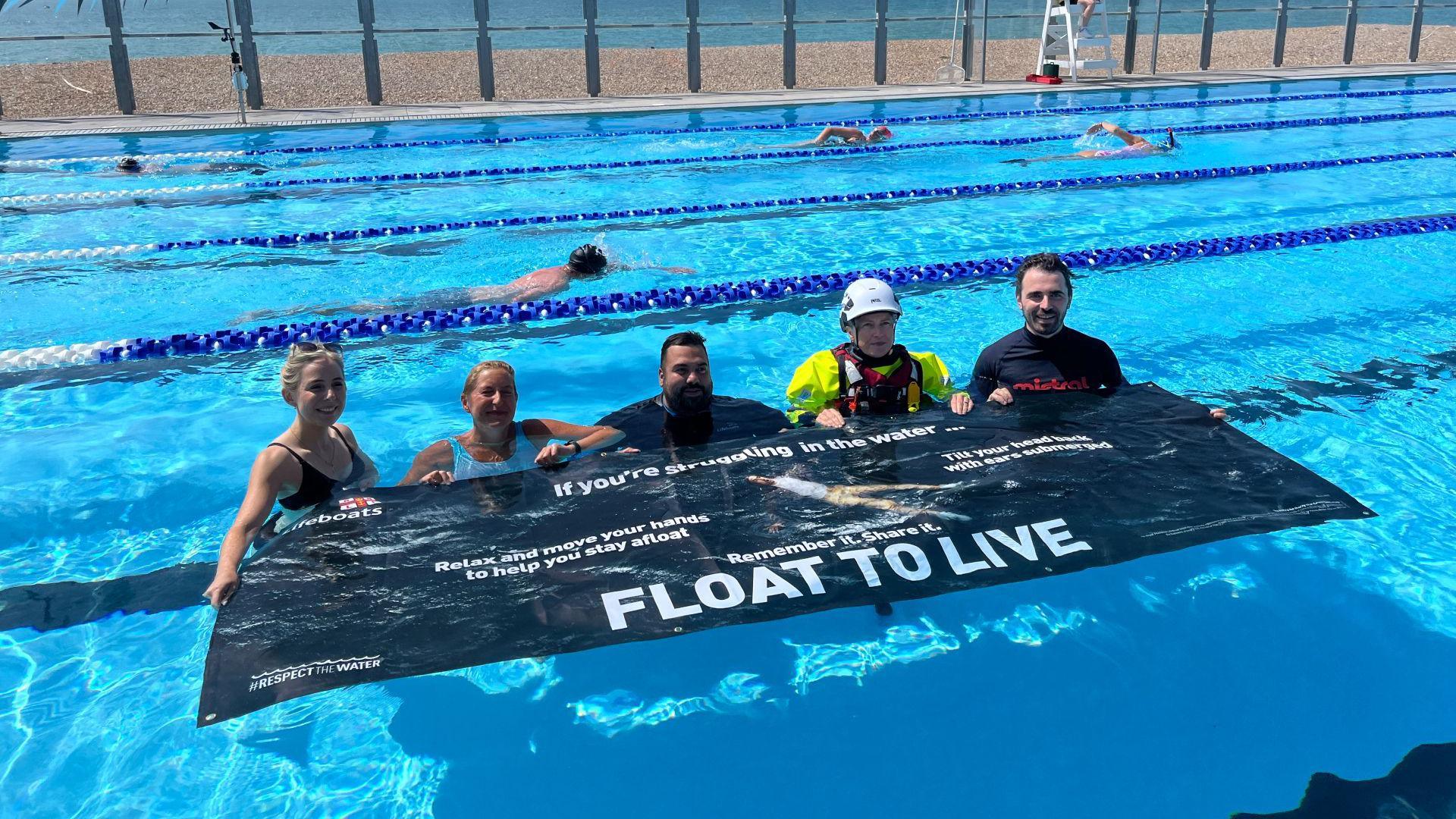 A group of people in a swimming pool with a banner reading float to live. 