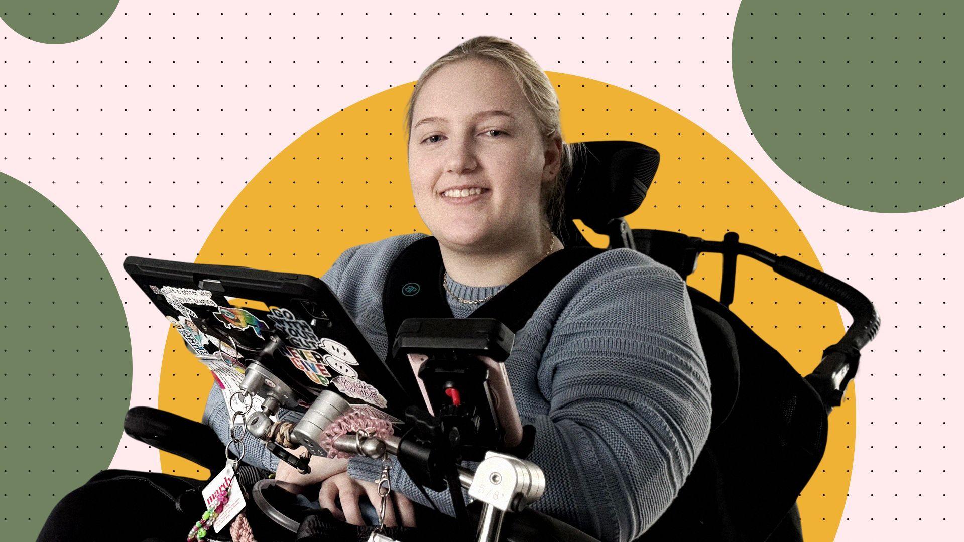 Evie sitting in an electronic wheelchair with a tablet attached is smiling 