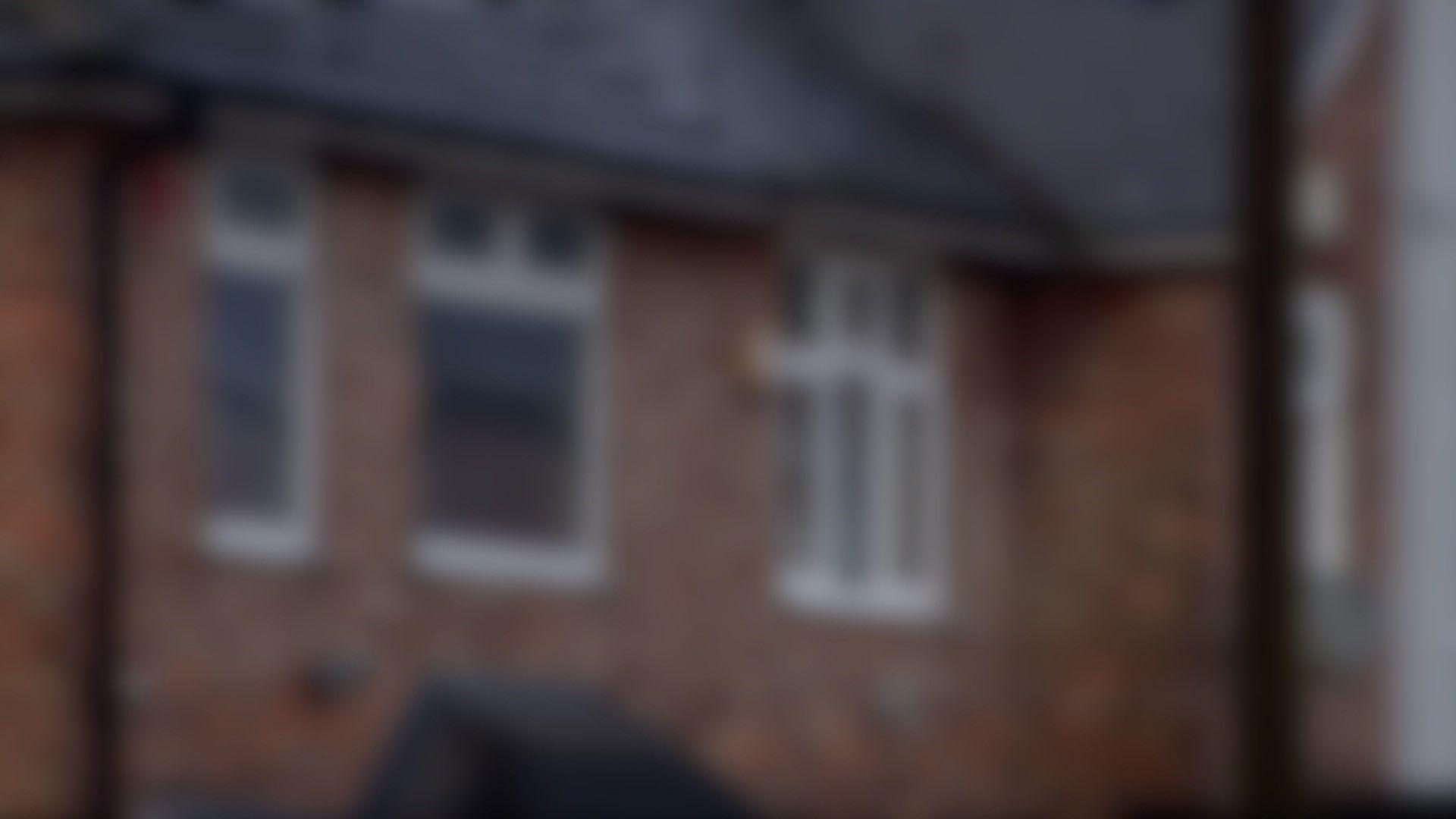 A blurred image of a house. It is red brick with white around the windows.