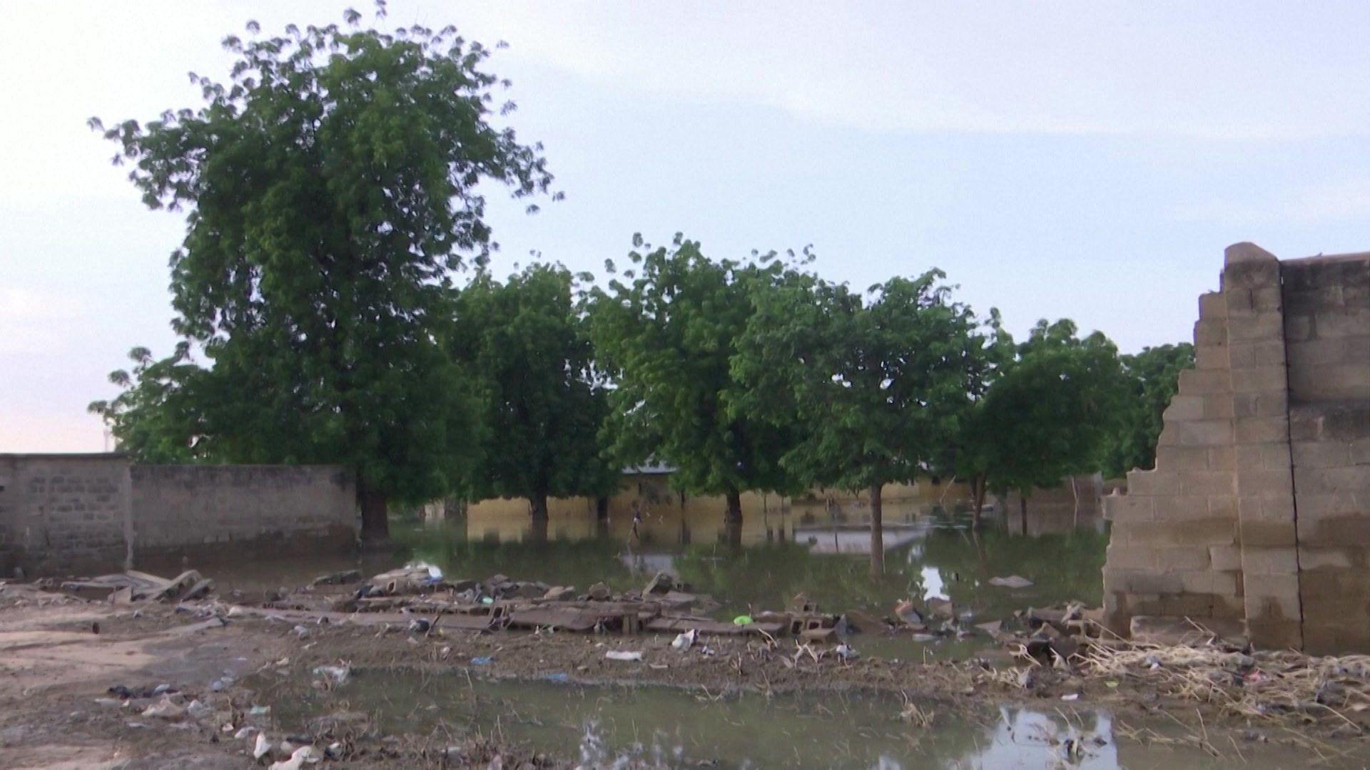 The collapsed wall of a compound near floodwater