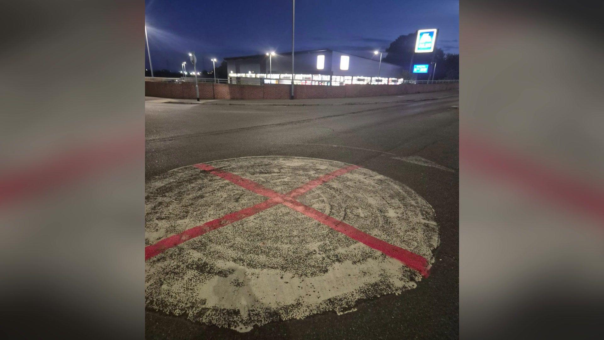 A red cross painted over a white roundabout. The night is dark.