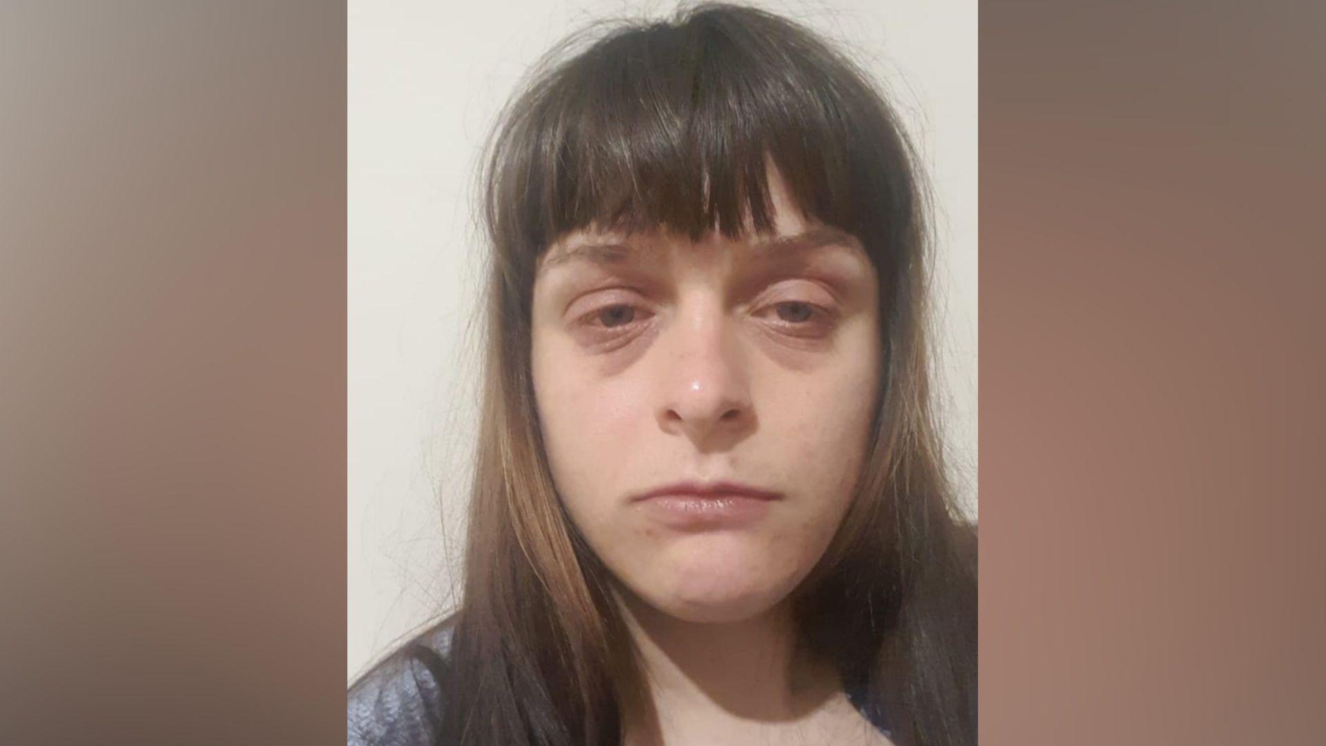 A selfie of a woman with long brown hair and a fringe over her forehead. She is not smiling and has dark bags under her eyes.