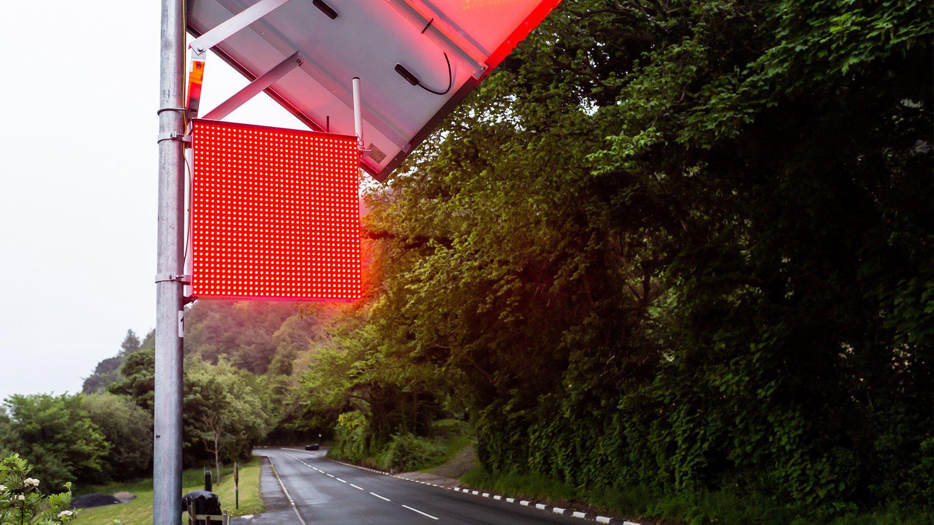 The LED flag system illuminated in red. A road can be seen below it with trees on the right-hand side.