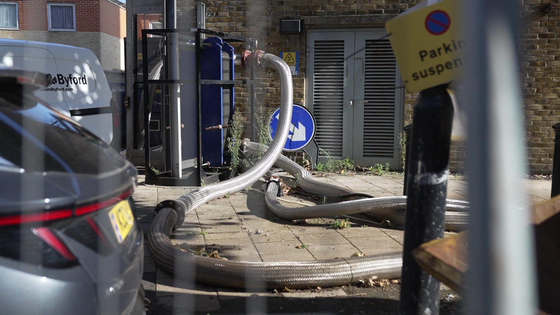 The network of North Peckham Heat Network pipes criss cross on the pavement in front of a boiler house