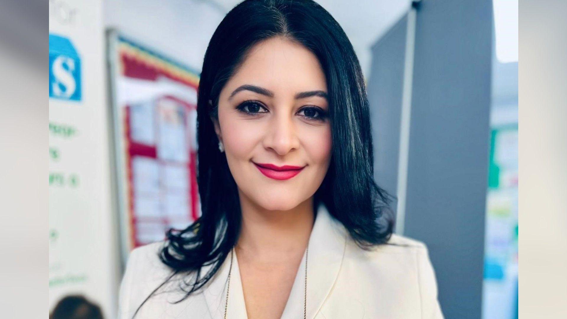 Shabina Asad Qayyum wearing a white suit, smiling for the camera. 