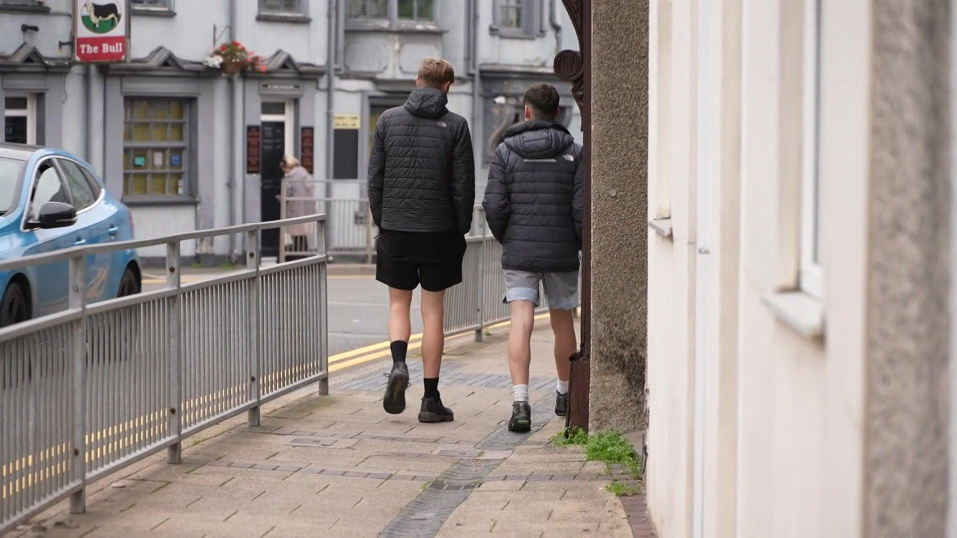 Dau lanc gyda'u cefnau tua'r camera yn cerdded ar hyd rhan o stryd fawr Bethesda