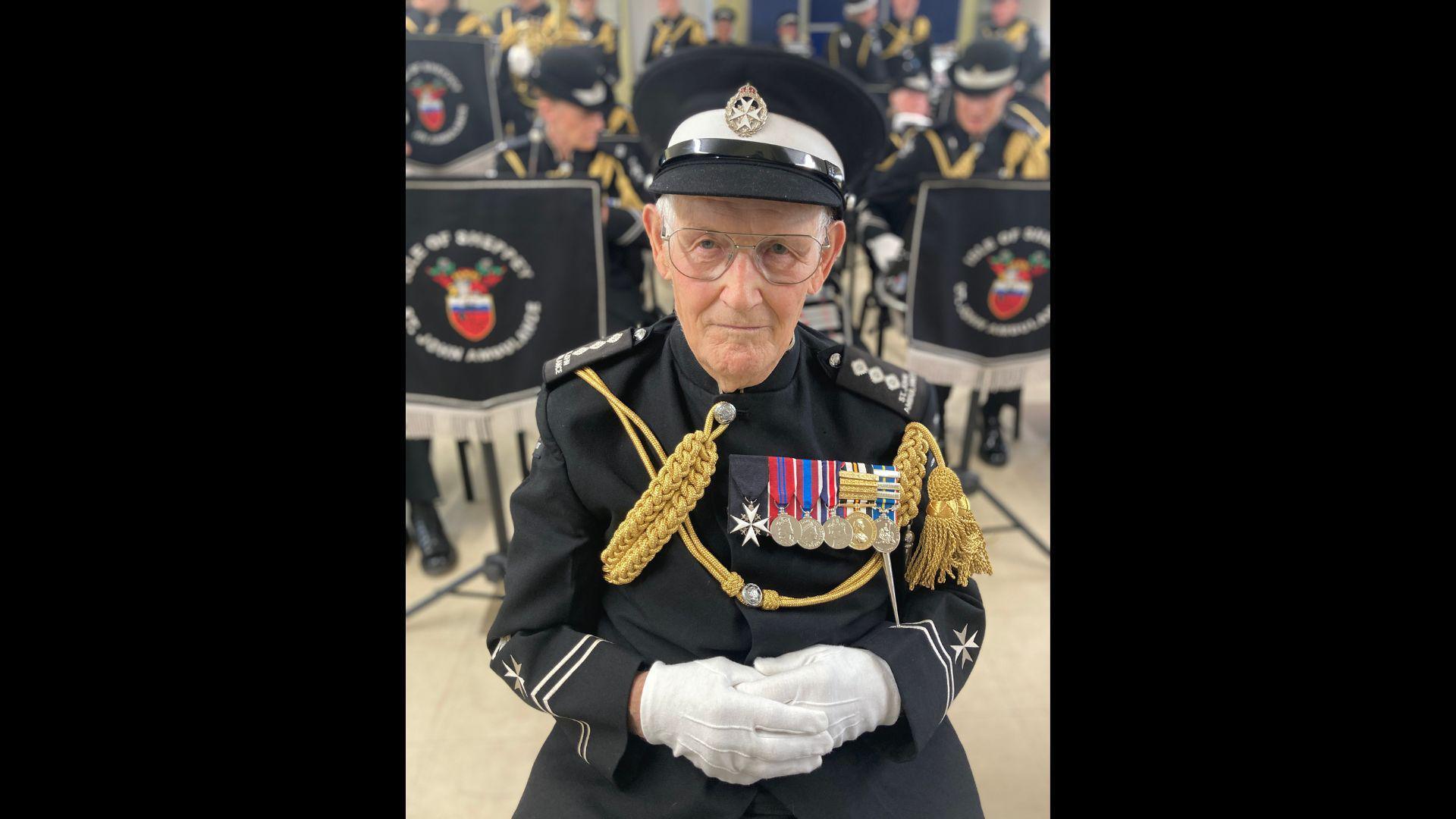 A St John Ambulance band member dressed in a black uniform, hat and white gloves.
